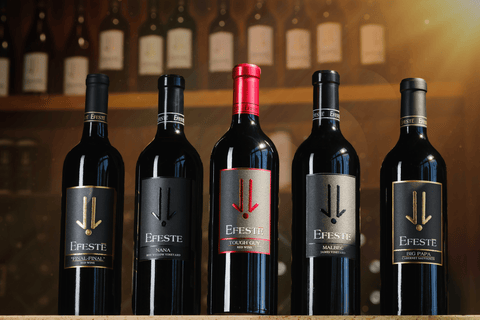 Five bottles of Efeste wine with a blurred background of more wine bottles.