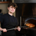 Man holding a pizza out of an oven in a kitchen setting