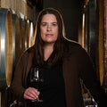 Woman holding a glass of wine in a winery setting with wine barrels.